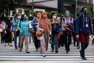 Diverse group of pedestrians wearing masks crossing a city crosswalk together.