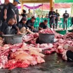 Group of volunteers in black shirts processing a large pile of raw meat under a tent. (informative)