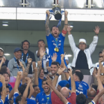 Athlete in blue jersey hoists a trophy above a cheering crowd at a sports victory celebration.