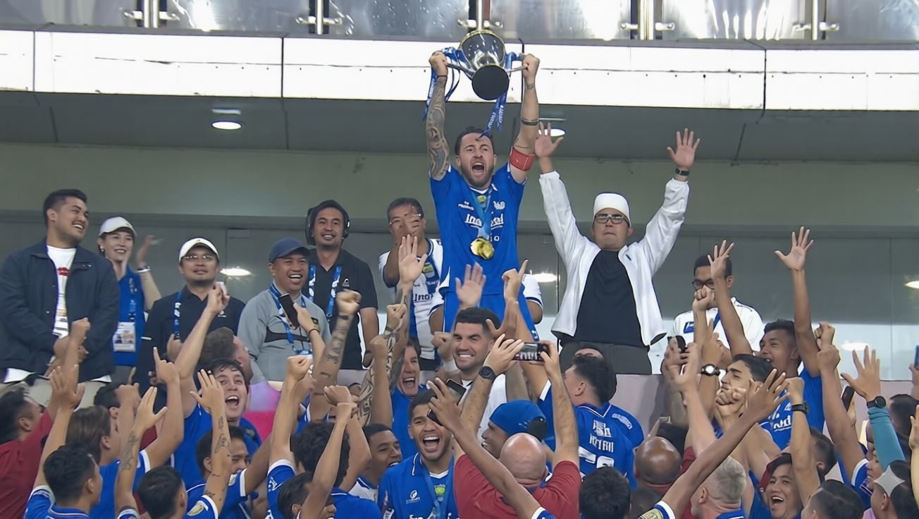 Athlete in blue jersey hoists a trophy above a cheering crowd at a sports victory celebration.