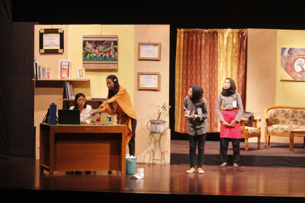Picture2 - Mabur.co Stage office scene: one woman seated at a desk with a laptop while another hands her something; two more women in hijabs observe nearby.