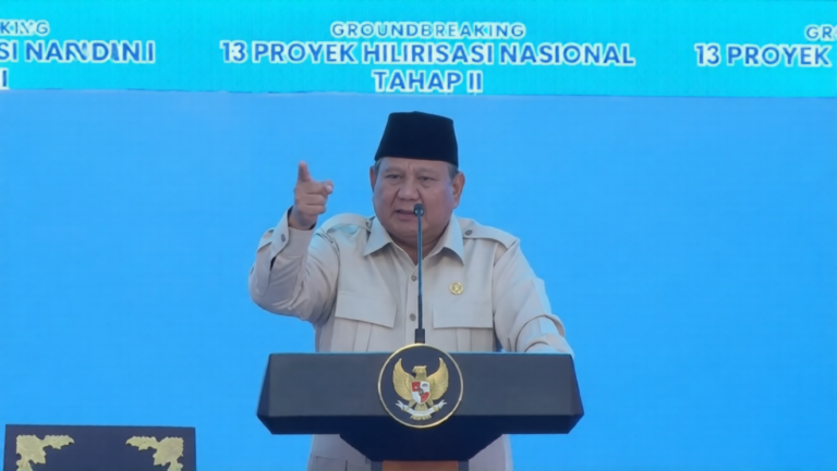 Government official delivering a speech at a podium during a national project groundbreaking event, blue backdrop with Indonesian emblems and signage
