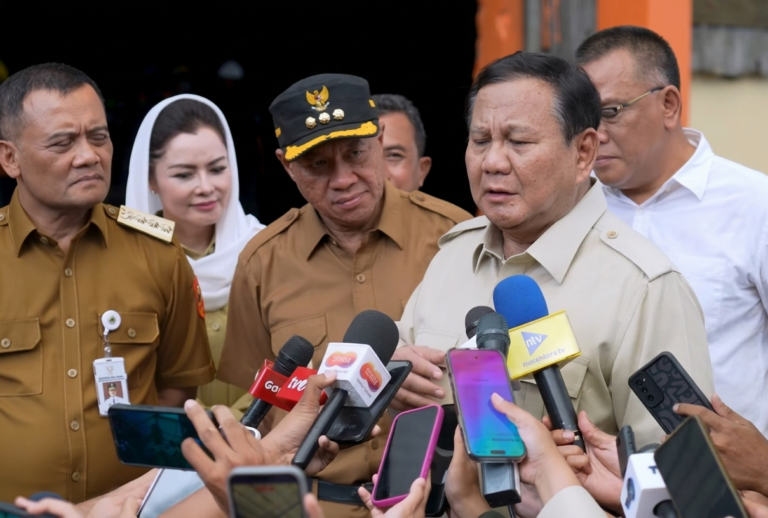 Man in beige uniform speaks to reporters as microphones surround him outside a building