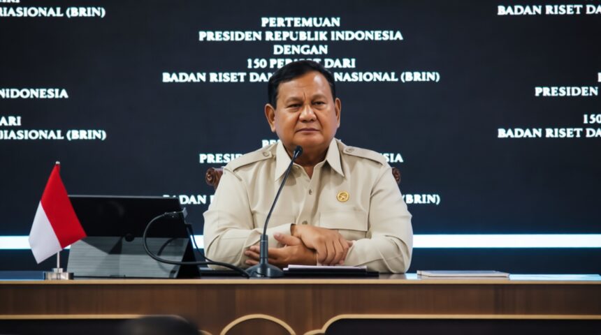 Indonesian official at a press conference, seated at a desk with a small flag and microphone, backdrop with white text in Indonesian