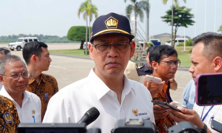 Purbaya by YT Liputan6 FIXX - Mabur.co Man in a white shirt and navy cap with an emblem is interviewed by reporters outdoors, microphones in the foreground.