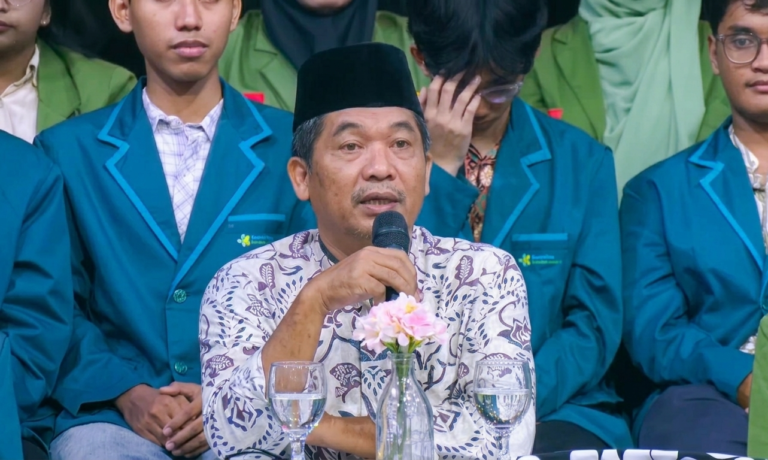 Direktur Eksekutif Lingkar Madani LIMA Ray Rangkuti by Kompas TV - Mabur.co Man in batik shirt and black cap speaks into a microphone at a formal event, with students in teal blazers around him and flowers on the table.