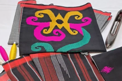 Black fabric with bright yellow and pink embroidery, placed on striped red-gray textiles with sewing tools nearby.