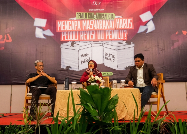 Panel discussion with three speakers on a stage; banner behind asks why society should care about electoral law revisions (Indonesian text).
