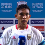 Footballer in white kit being interviewed with a blue Hyundai microphone, backdrop shows ASEAN Championship logos and sponsor banners.
