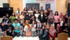 Group of about 40 people posing with books in a hall, a banner behind them indicating a national anthology event in Indonesian.