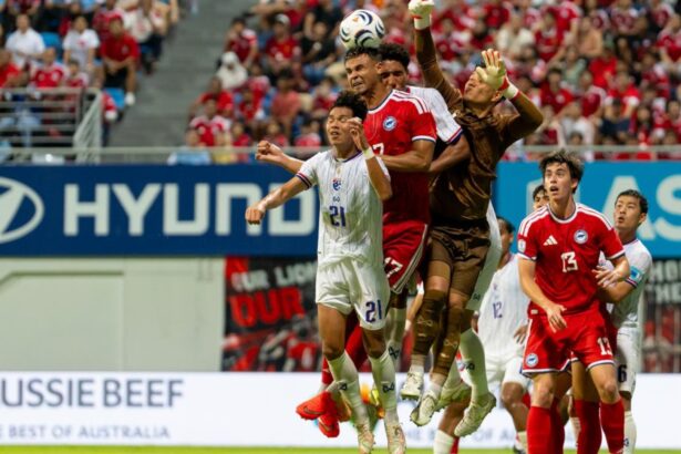 Soccer players jump to head the ball during a match with a cheering crowd in the stands behind them.