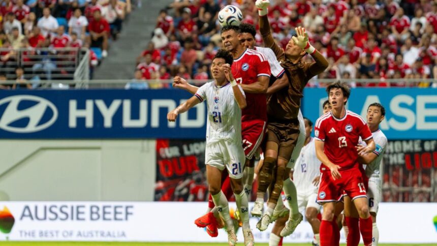 Soccer players jump to head the ball during a match with a cheering crowd in the stands behind them.