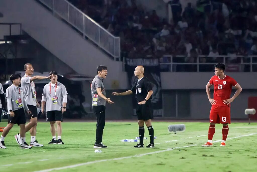 STY AFF 2024 by ANTARA - Mabur.co Soccer field scene with a coach arguing with the referee while a red-clad player watches nearby on the right; other staff and players stand in the background.