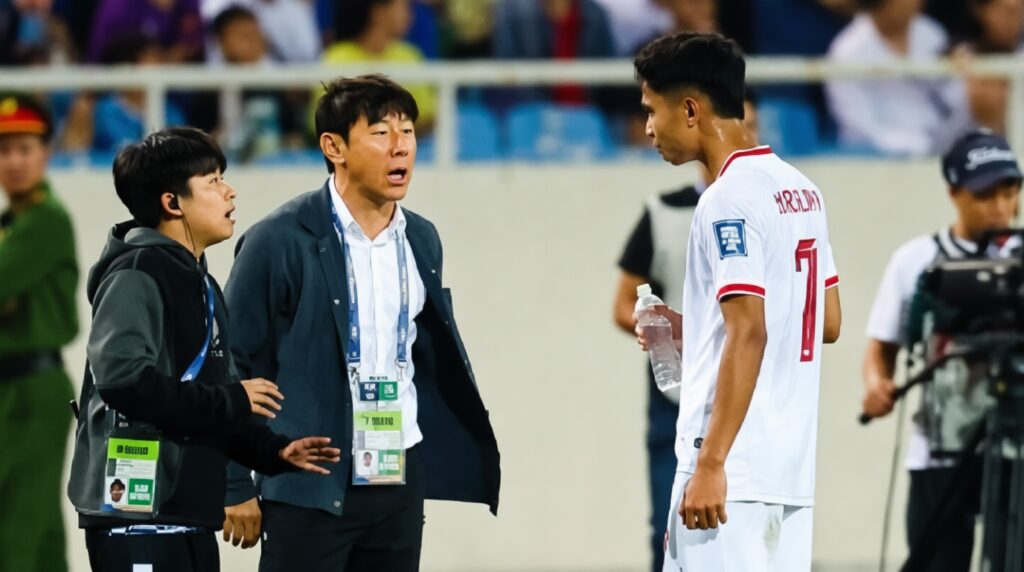 Two men with lanyards and a sports player in a white jersey face off on a field, one gesturing emphatically at the other edge of the frame