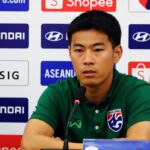 Asian male footballer in green polo speaking at a press conference with logos (Hyundai, Shopee, ASEAN) in the background and a soccer ball on the left.