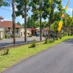 Street view of a village main road with a cream building and red-tiled roof on the left, and colorful flags along the road on a sunny day