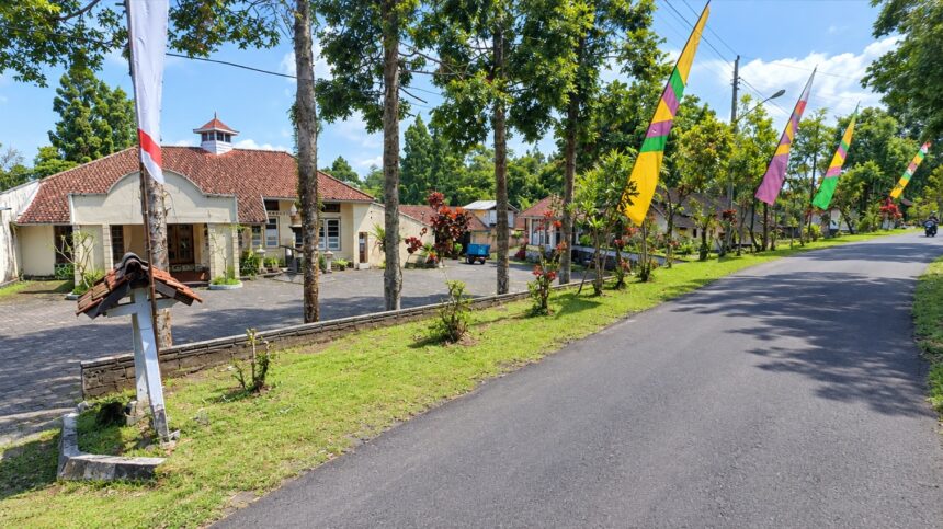Street view of a village main road with a cream building and red-tiled roof on the left, and colorful flags along the road on a sunny day