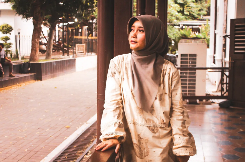 Screenshot 2026-06-01 at 21-34-15 6 Instagram - Mabur.co Woman wearing a hijab standing outdoors by a railing, gazing off to the side with a thoughtful expression.