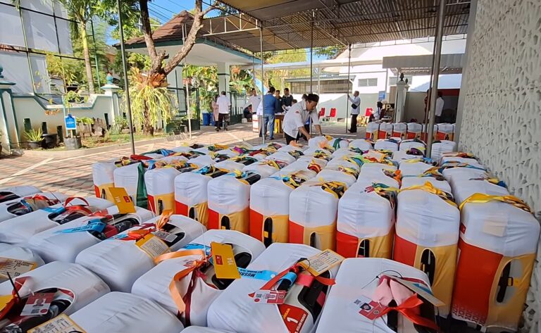 Rows of ready-to-distribute gift bags under a canopy at an outdoor community event; volunteers organizing them.