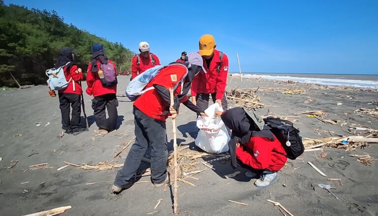 Group of volunteers in red jackets collecting litter along a sandy beach