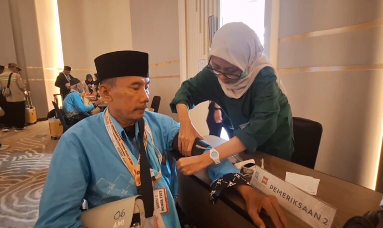 Healthcare worker in a hijab checks an elderly man's blood pressure with a cuff at a health event set-up in a conference area.