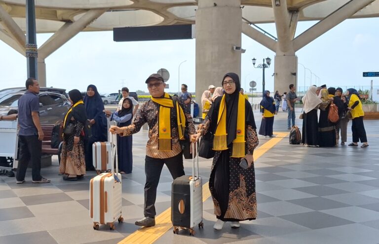Group of travelers with yellow scarves walking through a modern airport terminal with luggage in tow under a concrete canopy.