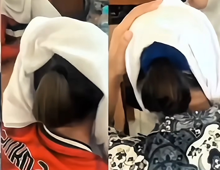 Two people seated, white cloths draped over their heads as they bend forward; one in red and the other in a blue patterned top.