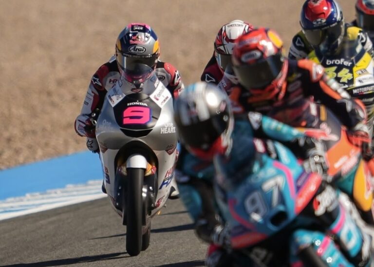 Motorcycle racers on a track in a close chase, rider with pink number 5 leading the pack on a silver bike.