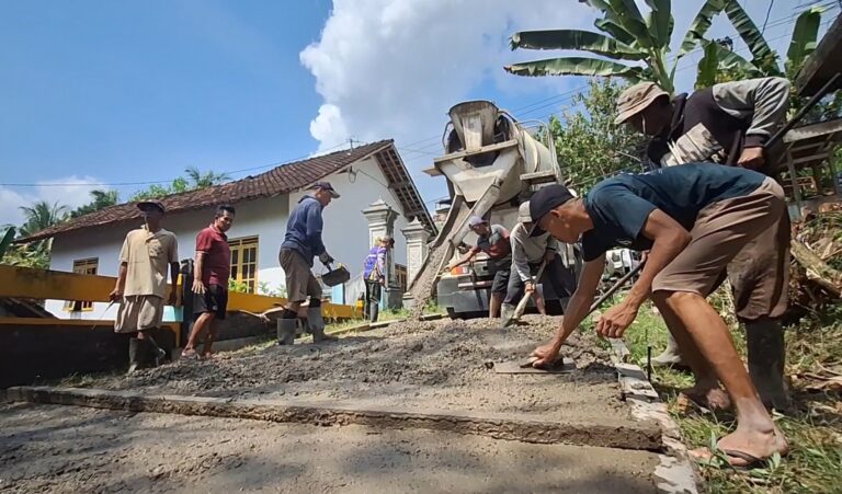Group of workers repaving a small road in a rural neighborhood, using a concrete mixer and shovels while a few men help spread gravel and level the surface.
