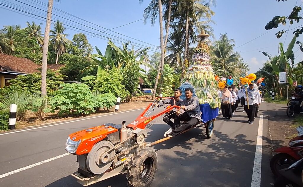 Screenshot_20260520_185914_Gallery - Mabur.co Parade on a sunny rural road with an orange tractor pulling a leaf-covered festival float and marchers behind it.