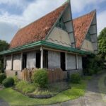 Two pointed-roof house with red clay tiles, green trim, and a small garden in front