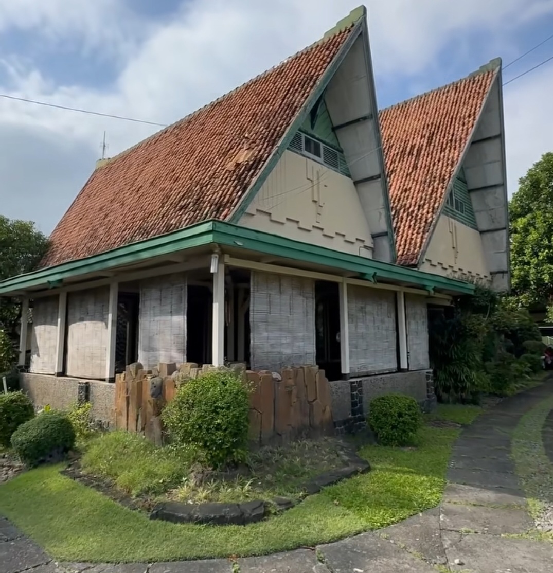 Two pointed-roof house with red clay tiles, green trim, and a small garden in front