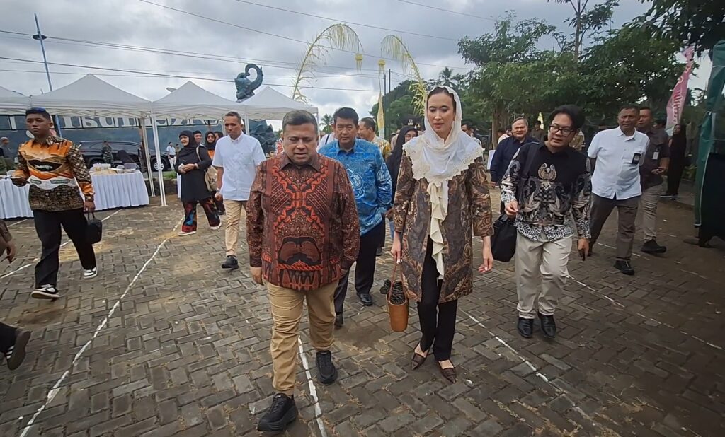 A group of people in batik clothing walking along a brick-paved path at an outdoor event with white tents in the background.