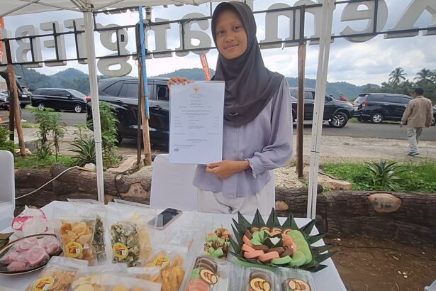 Woman in hijab displaying a certificate at an outdoor market booth with snacks on the table.",