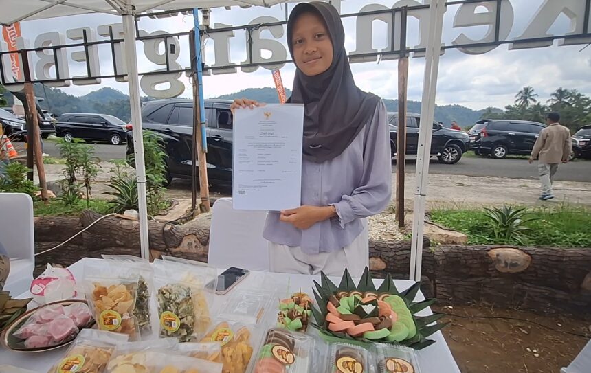 Screenshot_20260531_153755_Gallery - Mabur.co Woman in hijab displaying a certificate at an outdoor market booth with snacks on the table.",