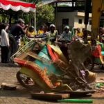 People gathered outdoors under a red-and-white striped canopy, with colorful pedal boats and debris on the ground in a festival-like scene.