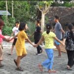 Group of children and teenagers forming a circle by holding hands and playing a game in a village yard.