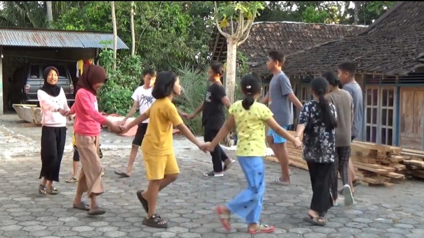 Group of children and teenagers forming a circle by holding hands and playing a game in a village yard.