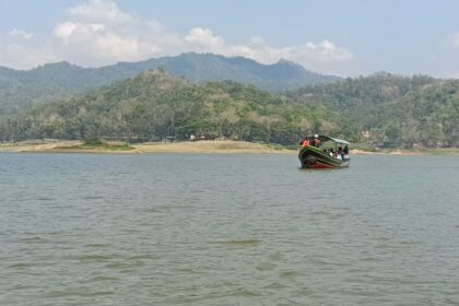 Colorful boat with passengers on a calm lake, forested hills beyond and a blue sky ahead.