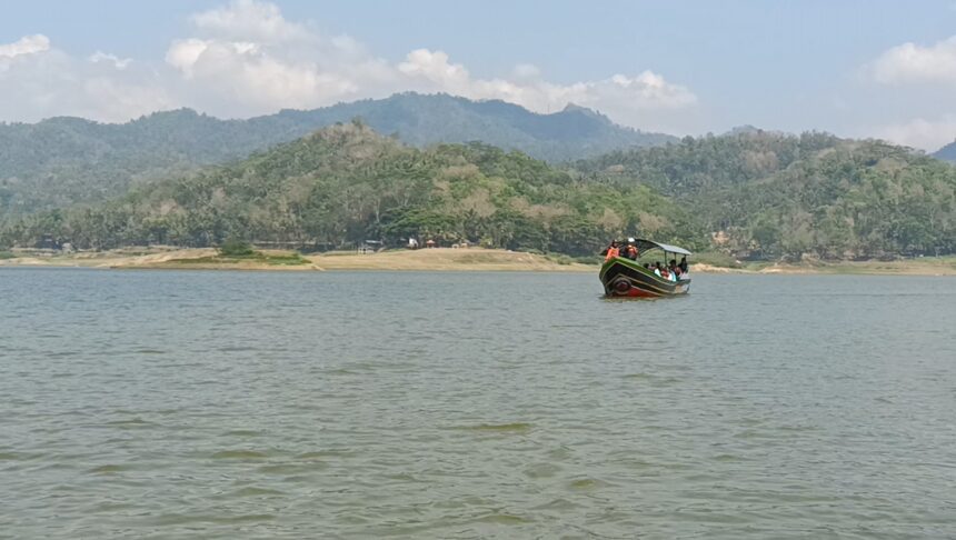 Screenshot_20260612_161414_Gallery - Mabur.co Colorful boat with passengers on a calm lake, forested hills beyond and a blue sky ahead.