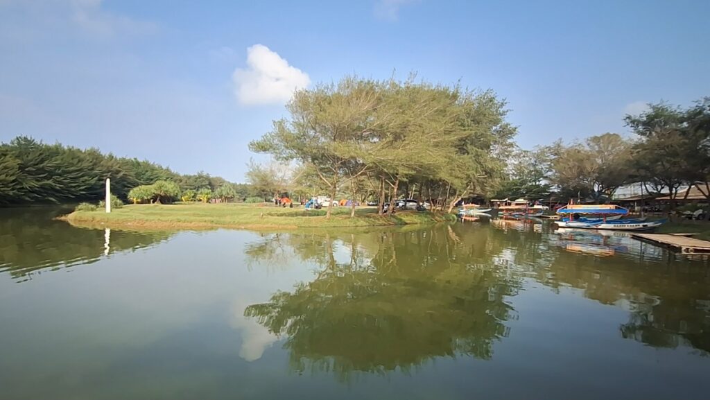 Screenshot_20260612_161941_Gallery - Mabur.co Calm lake in a park with a tree-lined shore and colorful boats docked along the right side.