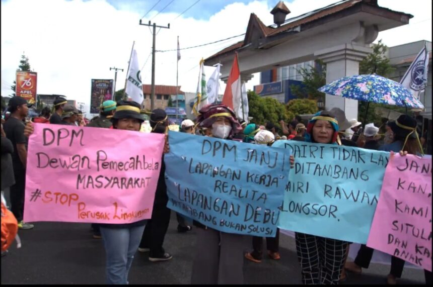 Screenshot_20260615_172945_X - Mabur.co Group of protesters marching on a street, holding colorful banners and flags, with an overhead structure in the background.