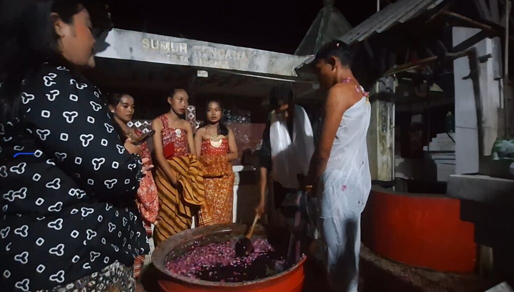 Screenshot_20260616_092417_Gallery - Mabur.co Group of people in colorful outfits gathered at night around bowls of pink flower petals, watching a ritual.