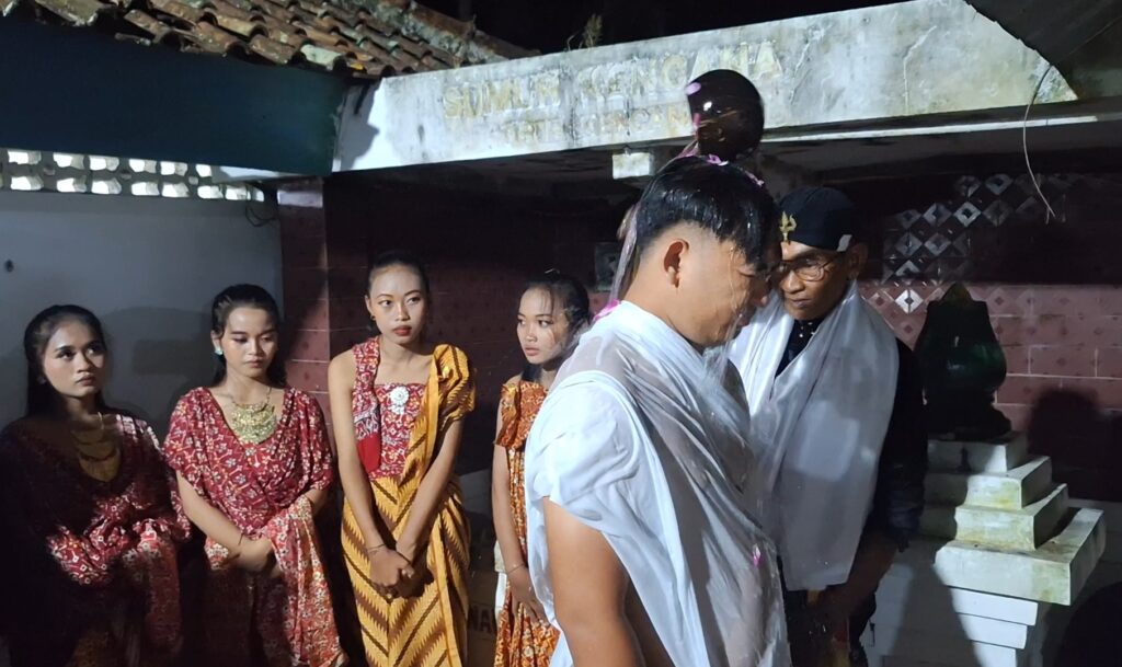 Screenshot_20260616_092450_Gallery - Mabur.co Group of five young people in traditional red and gold outfits watch a man in a white robe perform a ceremony at a temple-like setting at night.