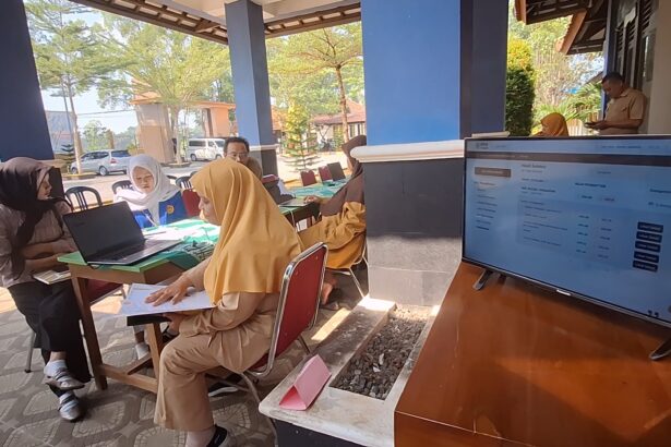 Group of people in hijabs seated at a table with a laptop and documents outside, engaging in a service or registration session at a booth.