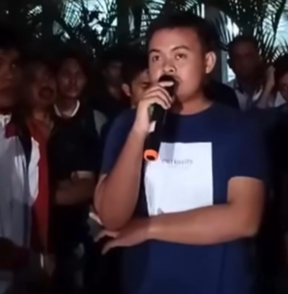 Screenshot_20260623_102335_Instagram - Mabur.co Person speaking into a microphone, holding a paper, in a crowded indoor/outdoor gathering at night.