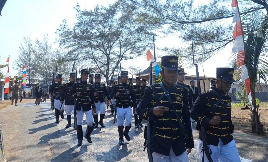 Soldiers march in a parade wearing black and gold uniforms with white trousers, carrying rifles; colorful flags line the street in the background.
