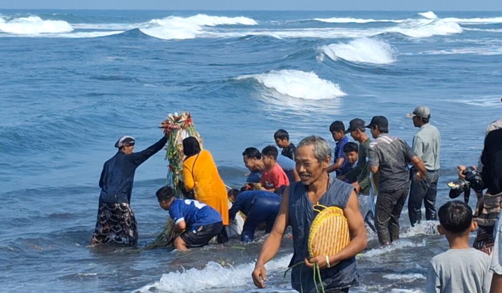 Group of people on a rocky beach releasing a flower wreath into the ocean during a ceremony