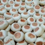 Pile of small white steamed buns with light brown tops in a basket.