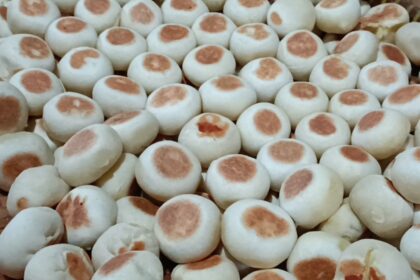 Pile of small white steamed buns with light brown tops in a basket.